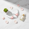 Flat lay of 3D red light EMS eye massager with serum and petals on marble