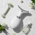 Flat lay of face and neck lift beauty device with flowers and serum