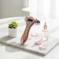 Flat lay of 4D EMS face massager roller on marble with serum and petals