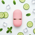 Flat lay of pink ice roller with ice cubes, cucumber and mint